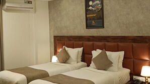 Ein Hotelzimmer mit zwei Betten, einem Deckenventilator, einer Klimaanlage, einem Gemälde und einem gemusterten Teppich.