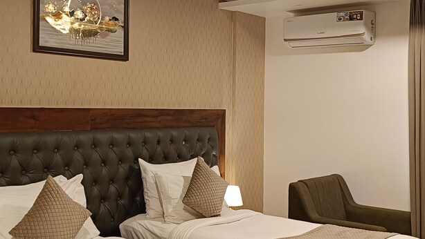 Ein Hotelzimmer mit einem großen Bett, einem kleineren Bett, einem Schreibtisch, einem Deckenventilator, einer Klimaanlage und einem gerahmten Bild an der Wand.