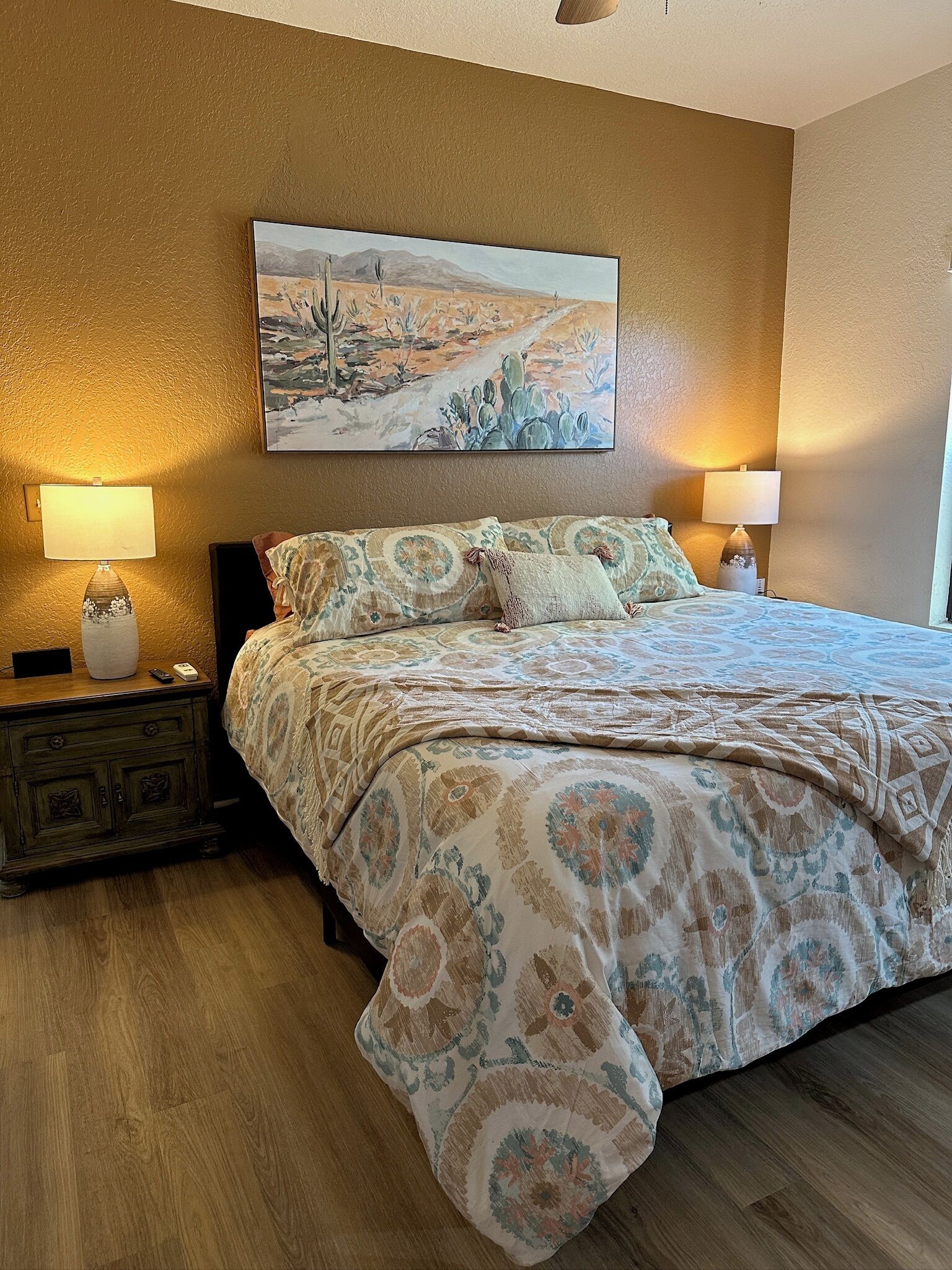 A bedroom with a large bed, two bedside lamps, a nightstand, and a painting on the wall.