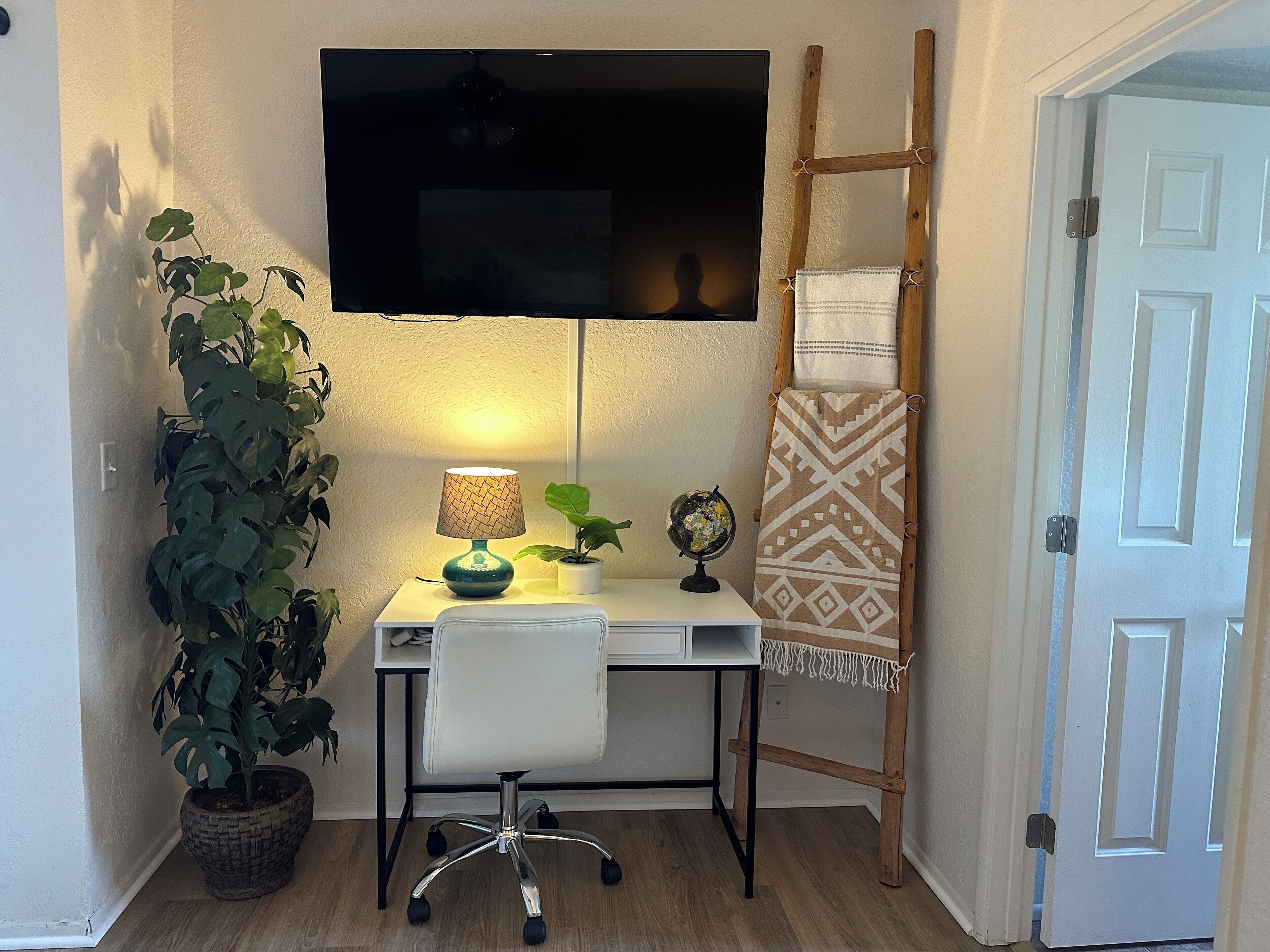 Un pequeño espacio de oficina con escritorio, silla, lámpara, planta en maceta, globo terráqueo y una escalera apoyada en la pared.