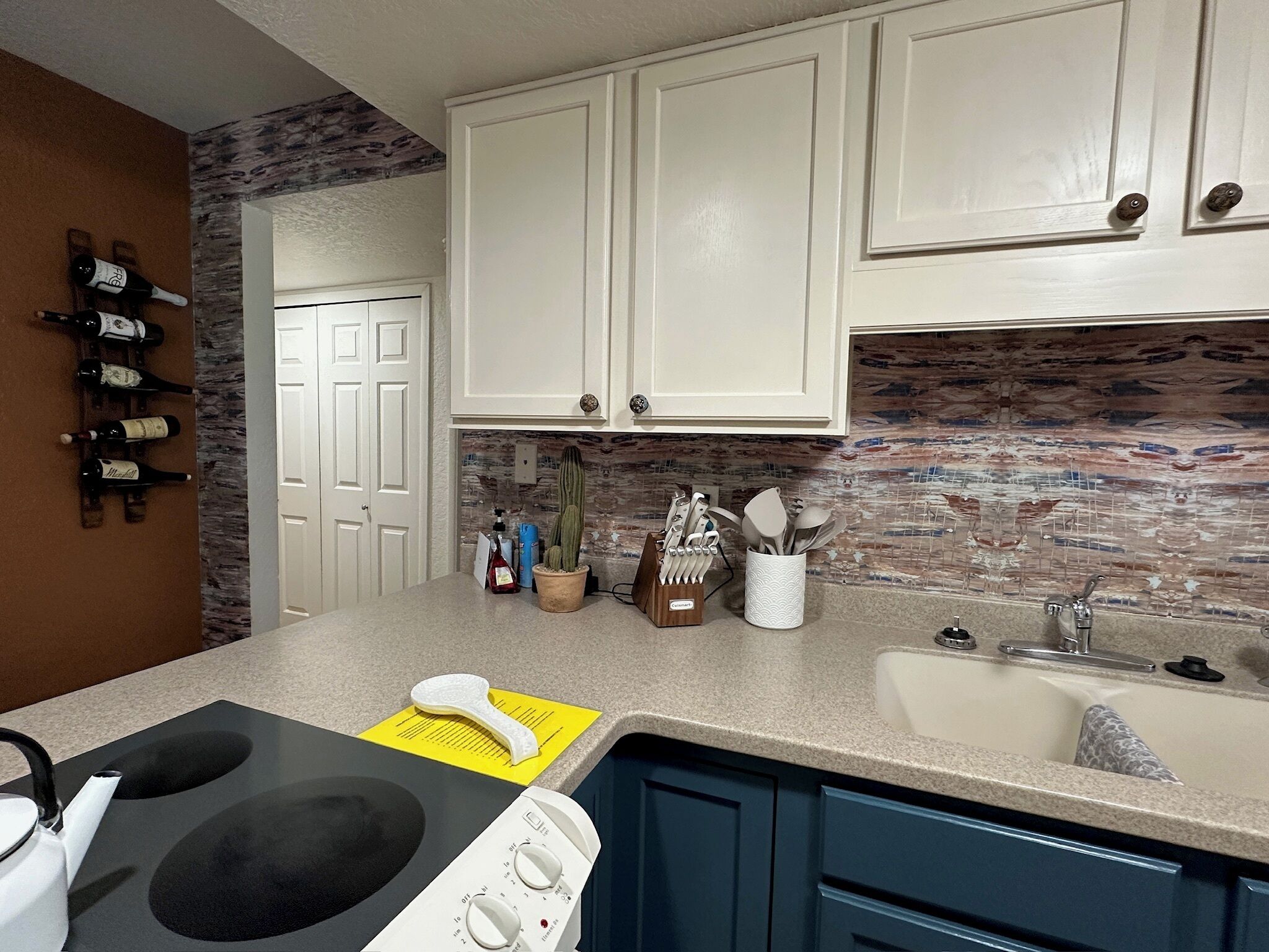 Una cocina con armarios blancos, encimera de granito, estufa integrada y salpicadero con diseño de mosaico.