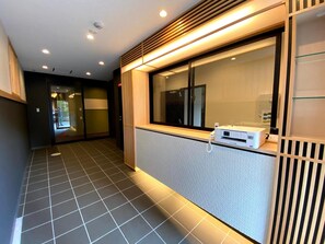 A hotel corridor with a reception area, a telephone, and a window with blinds.
