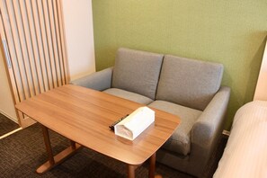 A small room with a wooden table, a grey sofa, and a green wall.