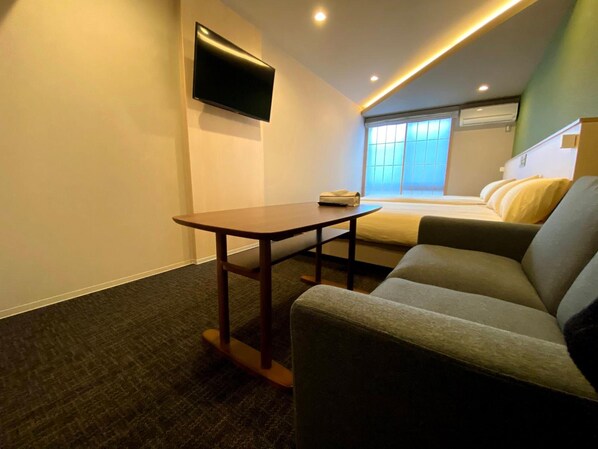 A compact hotel room with a bed, a sofa, a small table, and a TV mounted on the wall. - HIZ Hotel Gion-shirakawa (Kyoto)