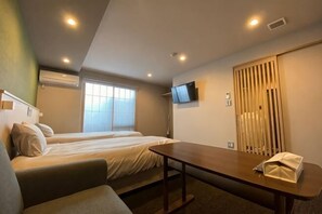 Une chambre d’hôtel avec deux lits, un canapé, une table, une télévision et une porte coulissante.