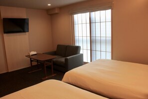 Une chambre d’hôtel avec un lit, une chaise, une petite table, un téléviseur fixé au mur et une fenêtre avec des stores.