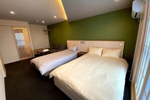 Une chambre d’hôtel avec deux lits, un canapé, un bureau et une fenêtre avec des stores.