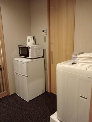 Una kitchenette compacta con microondas, refrigerador y lavadora.