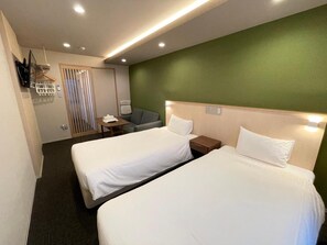 Ein Hotelzimmer mit zwei Betten, einem kleinen Tisch, einem Sessel und einem an der Wand befestigten Fernseher.