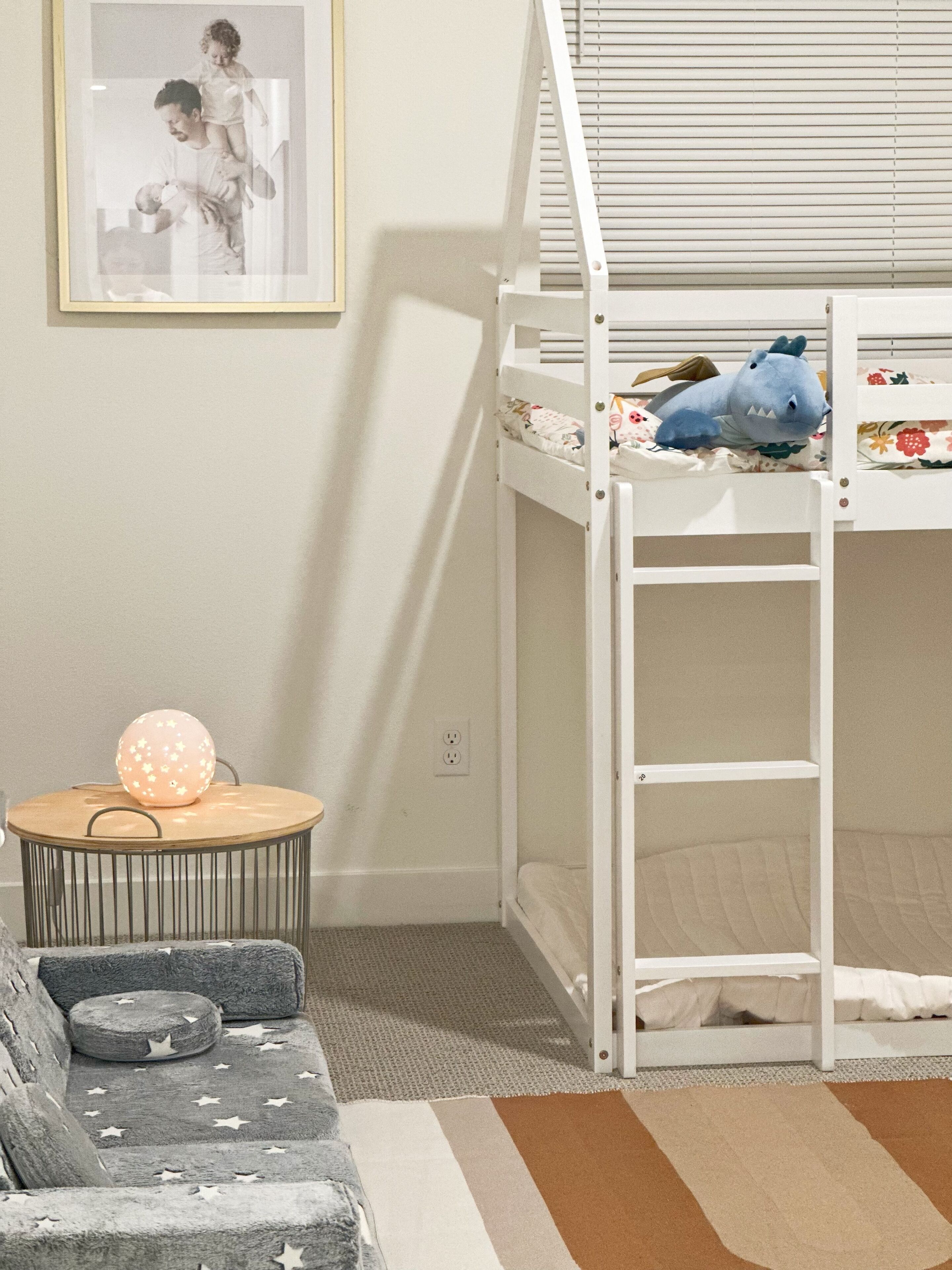 A child's bunk bed with a plush toy, a small round table with a star-patterned ball, and a grey sofa with star-patterned cushions.