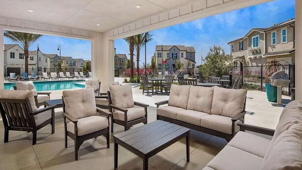 Zona de piscina con sillones de descanso, una mesa y vistas a un barrio residencial.