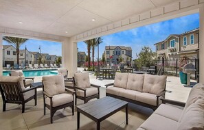 A poolside area with lounge chairs, a table, and a view of a residential neighborhood.