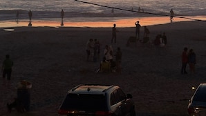 Escena de platja amb persones, un vehicle i un vaixell lluny.