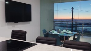 Una cuina moderna amb televisió de pantalla plana, zona de menjador amb vistes a l'oceà i un separador de vidre.
