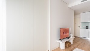 A modern, minimalist hallway with a flat-screen TV on a white console, a white door, and a white cabinet with a coffee machine.
