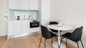 A modern kitchen with white cabinets, a built-in oven, and a round dining table with black chairs.