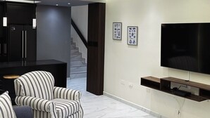 Una sala de estar moderna con un televisor de pantalla plana, sillones a rayas, un sofá de color oscuro y una escalera que conduce a otro nivel.