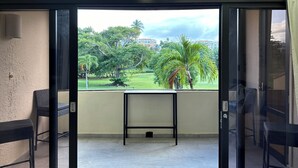 Un balcón con puerta de vidrio que da a una vista de un parque con árboles y un edificio al fondo.