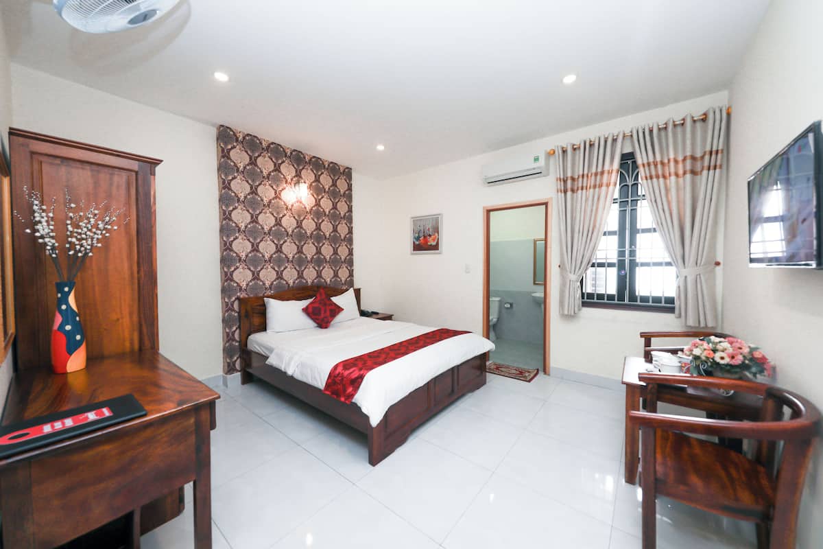 Une chambre d’hôtel avec un lit, un bureau, une chaise, une télévision et une salle de bain visible à travers une porte ouverte.
