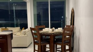 A dining area with a round table and chairs, a sofa, and a view through large windows. - Luxury Front View Beach House 3-bedroom with WiFi in Playas de Rosarito and more (Playas de Rosarito)