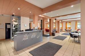 Un vestíbulo de hotel con recepción, zona de estar y vistas al comedor.