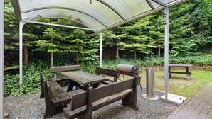 A covered outdoor seating area with benches and a grill. - Room 'Zimmer 23' with Shared Terrace, Shared Garden and Wi-Fi (Markt Erlbach)