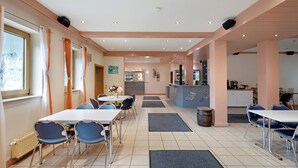 A hotel dining area with tables, chairs, a kitchen in the background, and a reception desk. - Room 'Zimmer 23' with Shared Terrace, Shared Garden and Wi-Fi (Markt Erlbach)