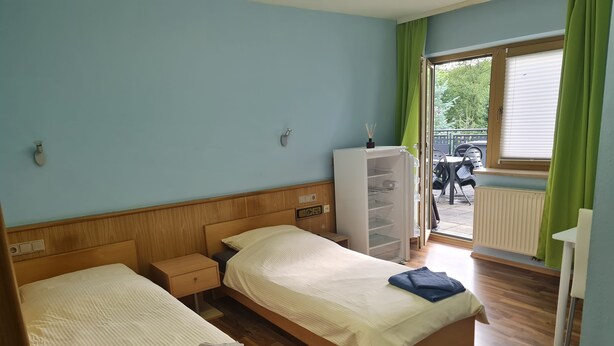 A hotel room with two beds, a wardrobe, a radiator, and a view of the outside. - Room 'Zimmer 23' with Shared Terrace, Shared Garden and Wi-Fi (Markt Erlbach)