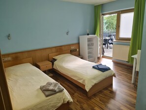 A hotel room with two beds, a wardrobe, a radiator, and a view of the outside.