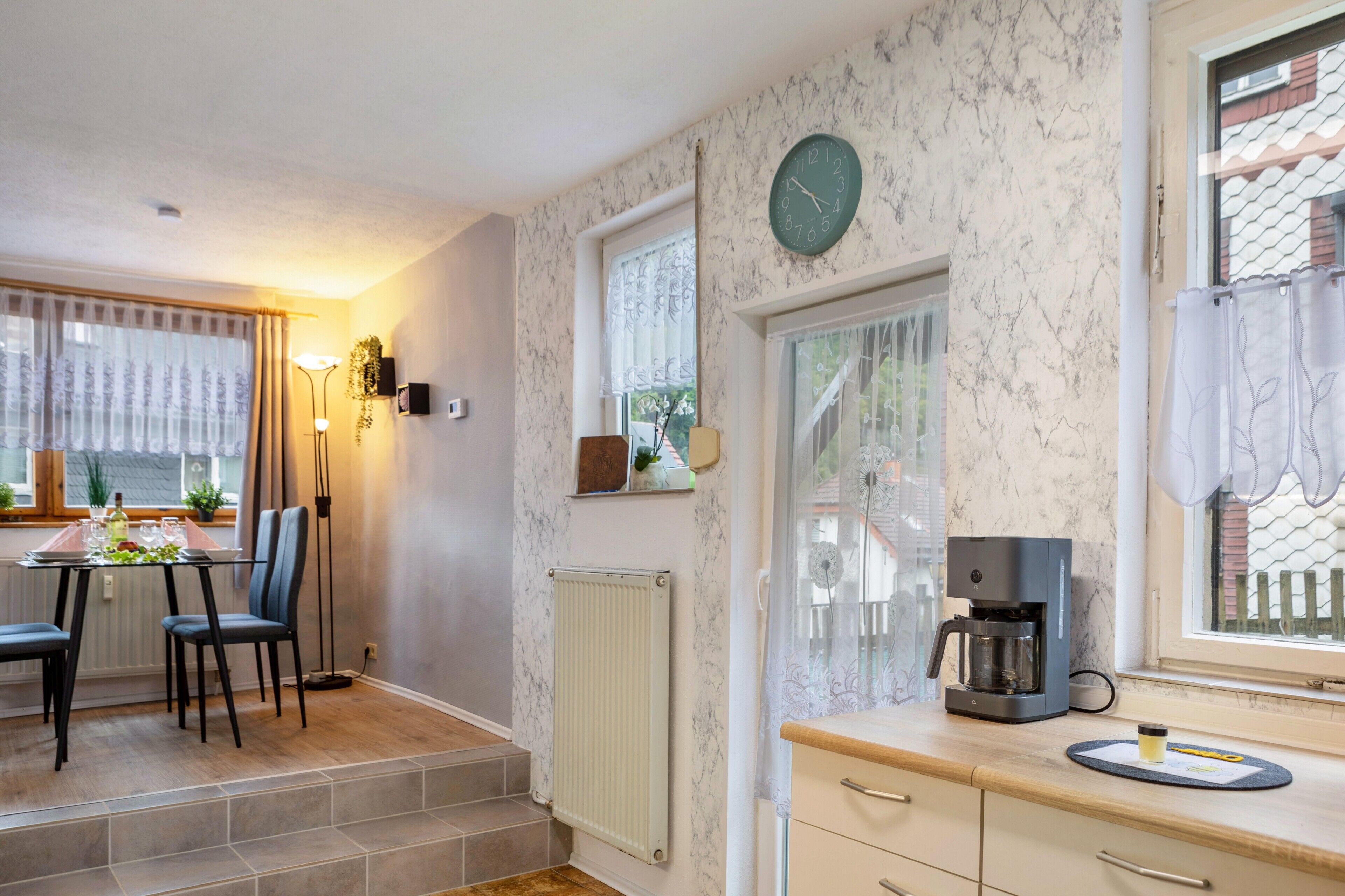 A kitchen with a coffee maker, a clock, and a dining area with chairs and a table.