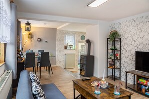Un salon comprenant un canapé, une table en bois, un meuble pour la télévision, une cheminée et, au fond, un coin repas.
