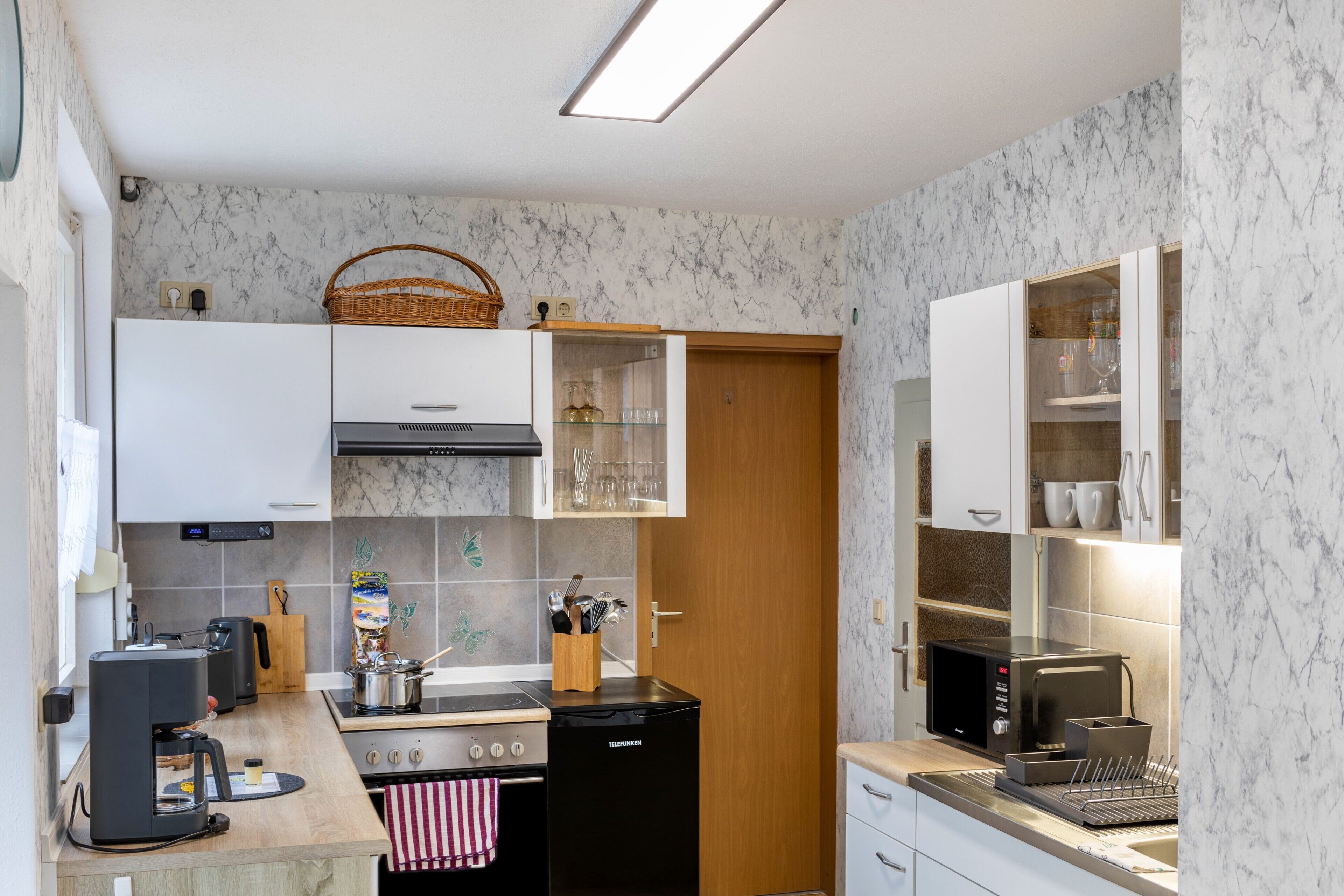A compact kitchen with a stove, microwave, and coffee maker, wooden cabinets, and a tiled backsplash.