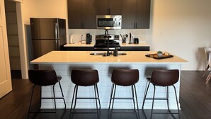 Uma cozinha moderna com ilha central, eletrodomésticos de aço inoxidável e armários de madeira escura.