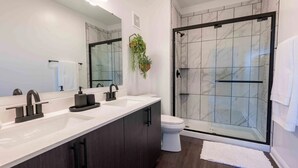 Uma casa de banho moderna com um espelho grande, duas pias, uma sanita e um chuveiro em cabine de vidro.