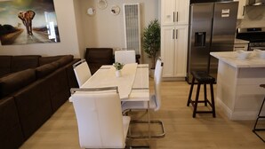 Una cucina moderna con un frigorifero in acciaio inossidabile, un tavolo da pranzo con sedie bianche e un divano in pelle marrone.