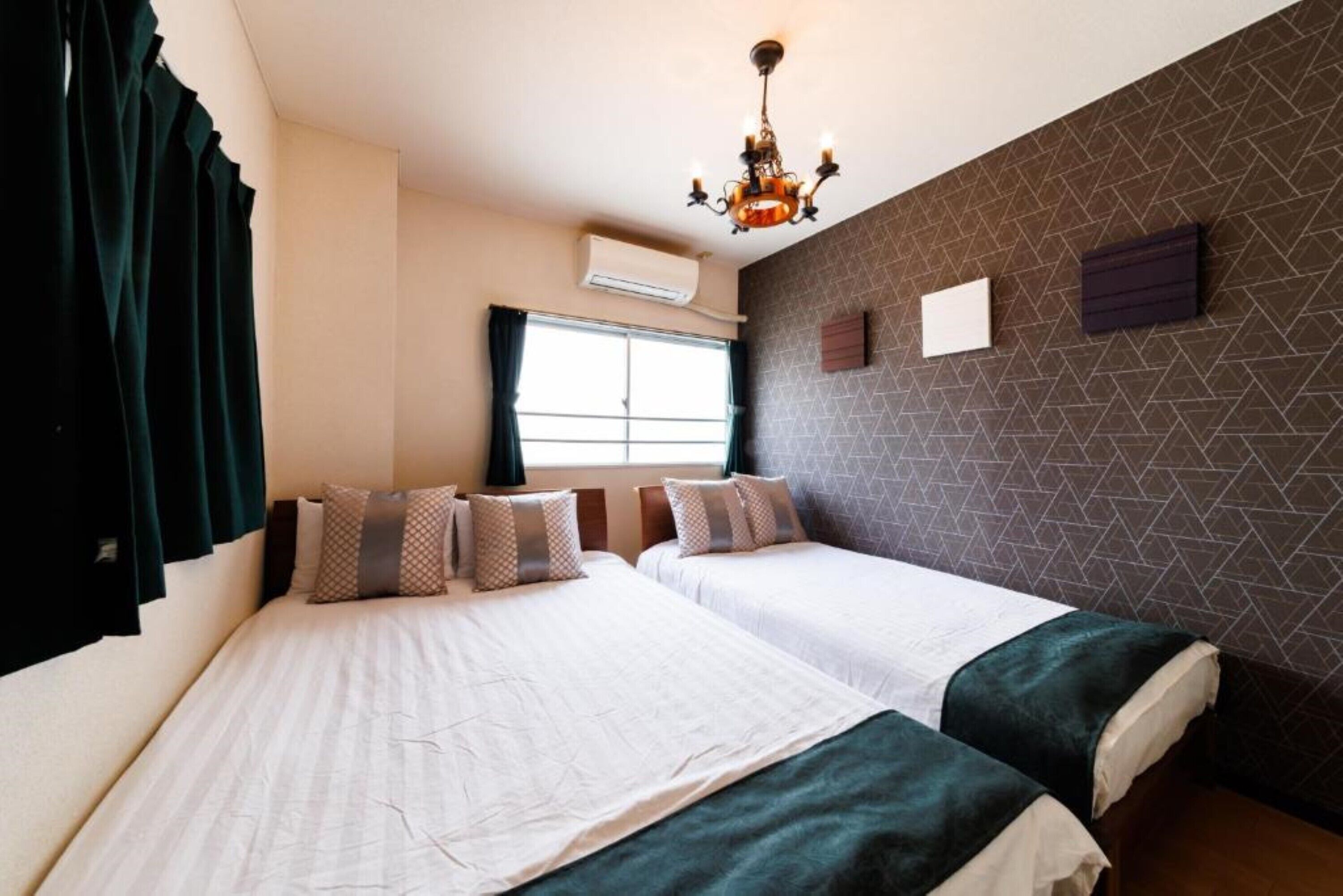Habitación de hotel con dos camas, una araña, un equipo de aire acondicionado y una pared con diseño geométrico.
