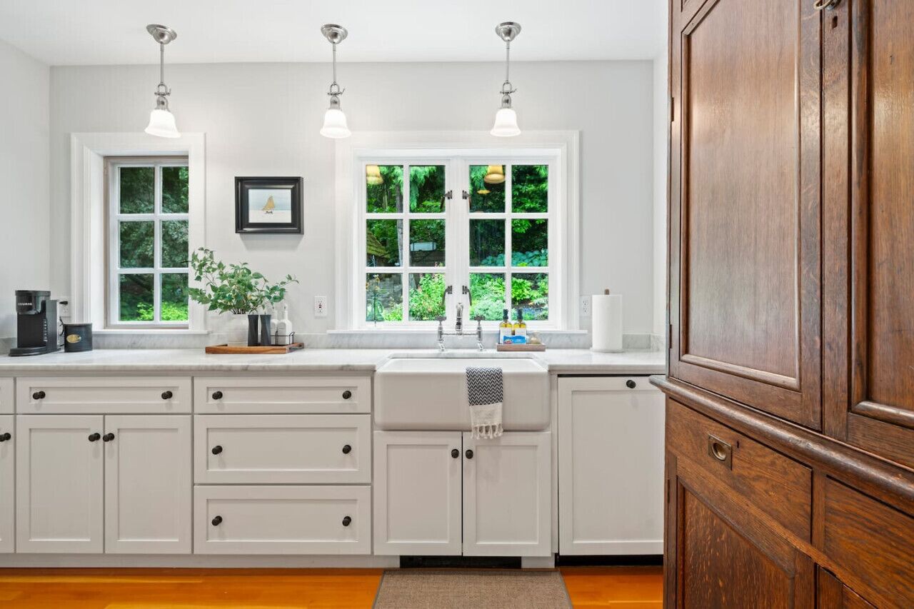 A kitchen with white cabinets, a sink, and a window with a view of greenery.