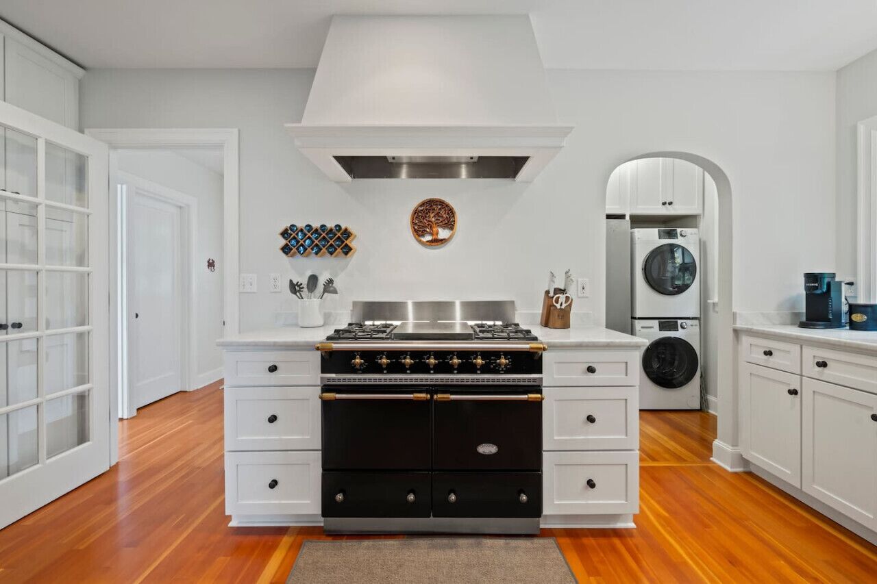 Una cocina con horno doble, estufa empotrada, campana de acero inoxidable, lavadora y cafetera.