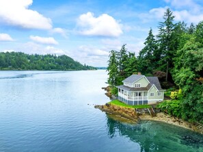Una casa en una propiedad junto al lago, con muelle, rodeada de un bosque frondoso y agua cristalina.