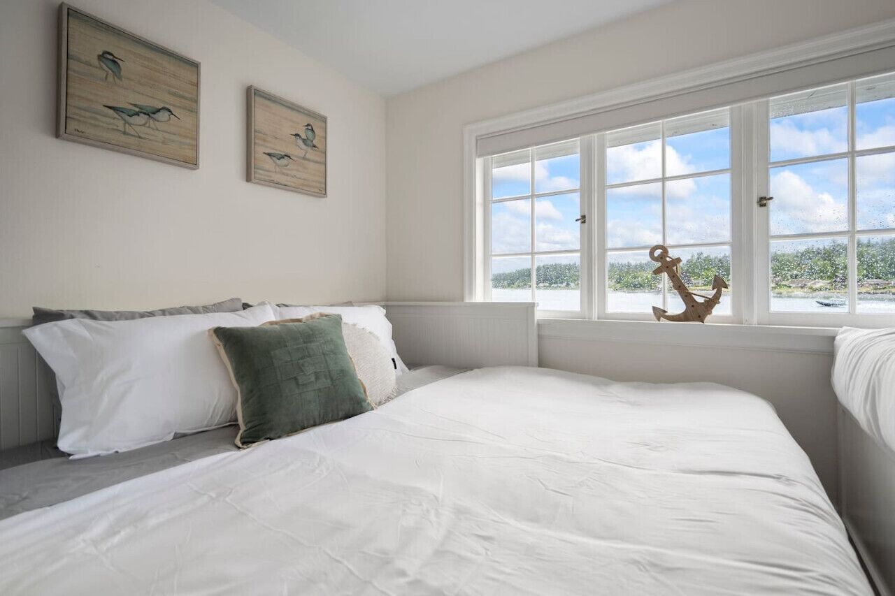 Ein Schlafzimmer mit einem großen Bett, einem Fenster mit Blick auf Bäume und zwei an der Wand befestigten Vogelgemälden.