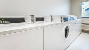 A modern laundry facility with multiple washing machines and dryers, a control panel, and a window with blinds. - Cozy 2 queen hotel in delightful Huntersville up to 4 people (Huntersville)