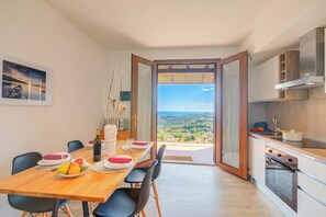 A modern kitchen with a view, a dining area with a table set for two, and a large window. - Il Vecchio Faggio: Lake Maggiore view Terrace, Gignese, Italy (Gignese)