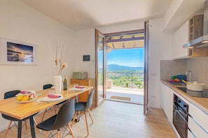 A modern kitchen with a view to the outdoors, a dining area with a table set for two, and a balcony with a scenic view.