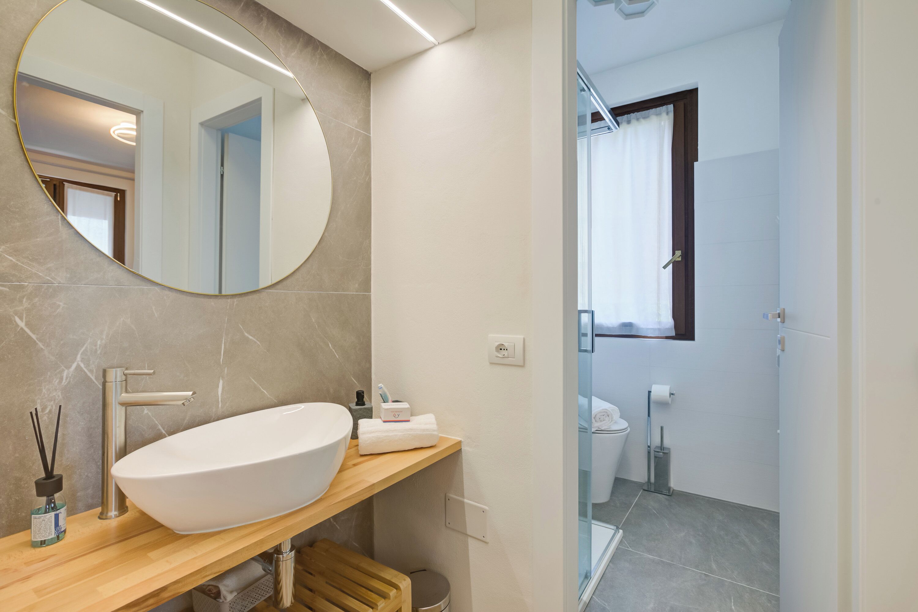 A modern bathroom with a large oval sink, a round mirror, and a wooden vanity.