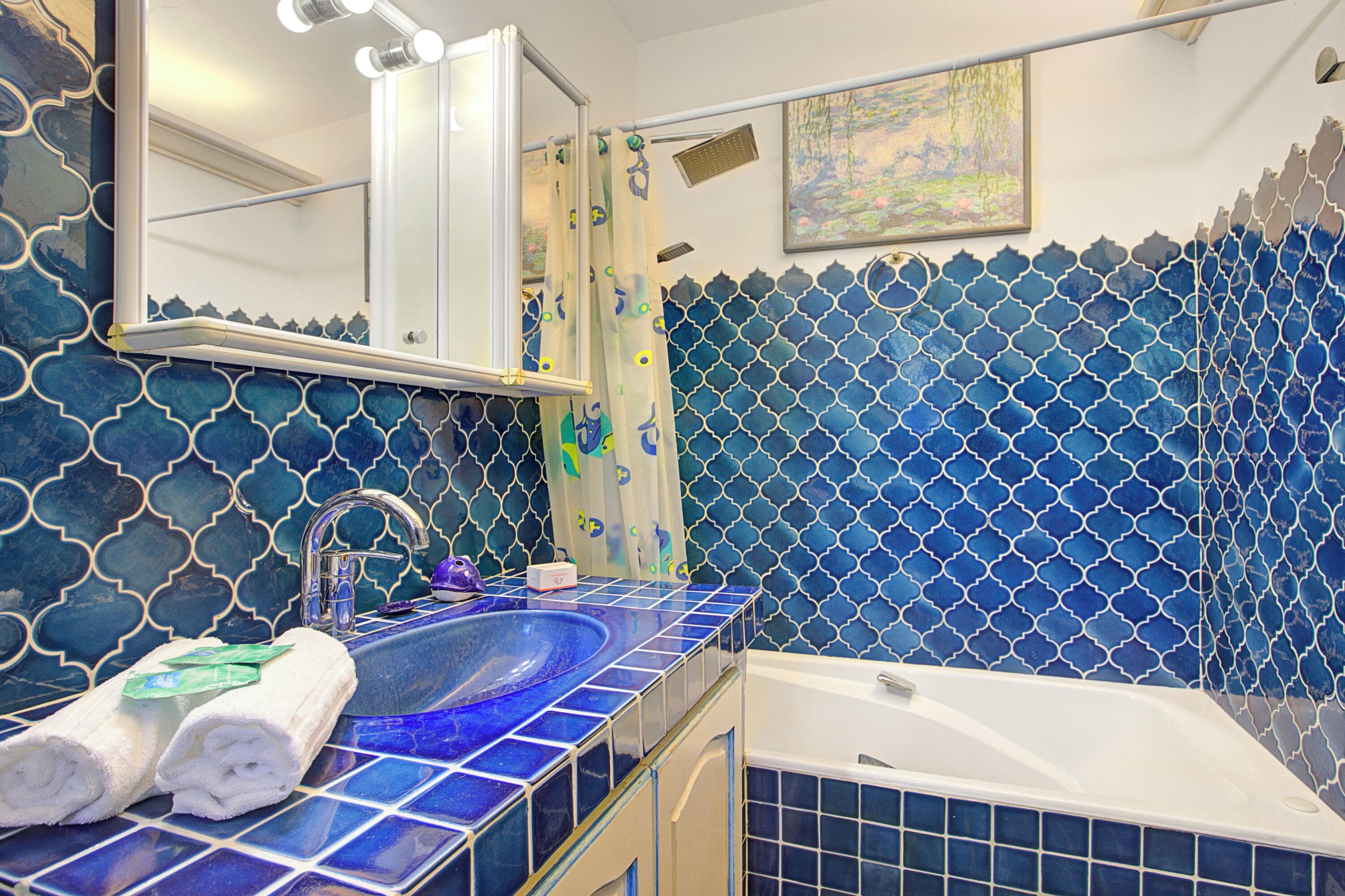 Une salle de bain avec un mur recouvert de carreaux bleus, un lavabo avec un miroir et une baignoire.
