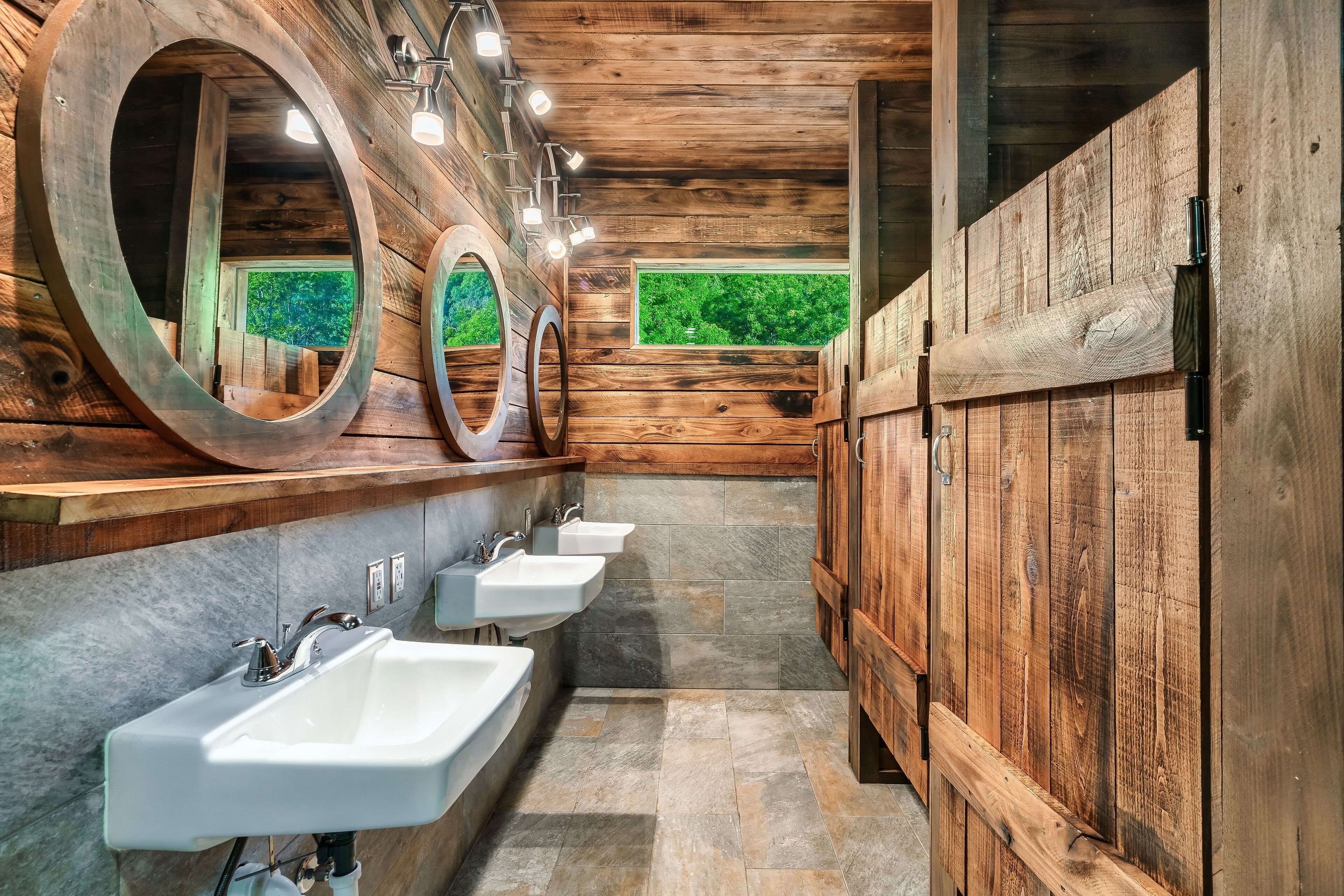 A wooden bathroom with three sinks, large mirrors, and a view of greenery.