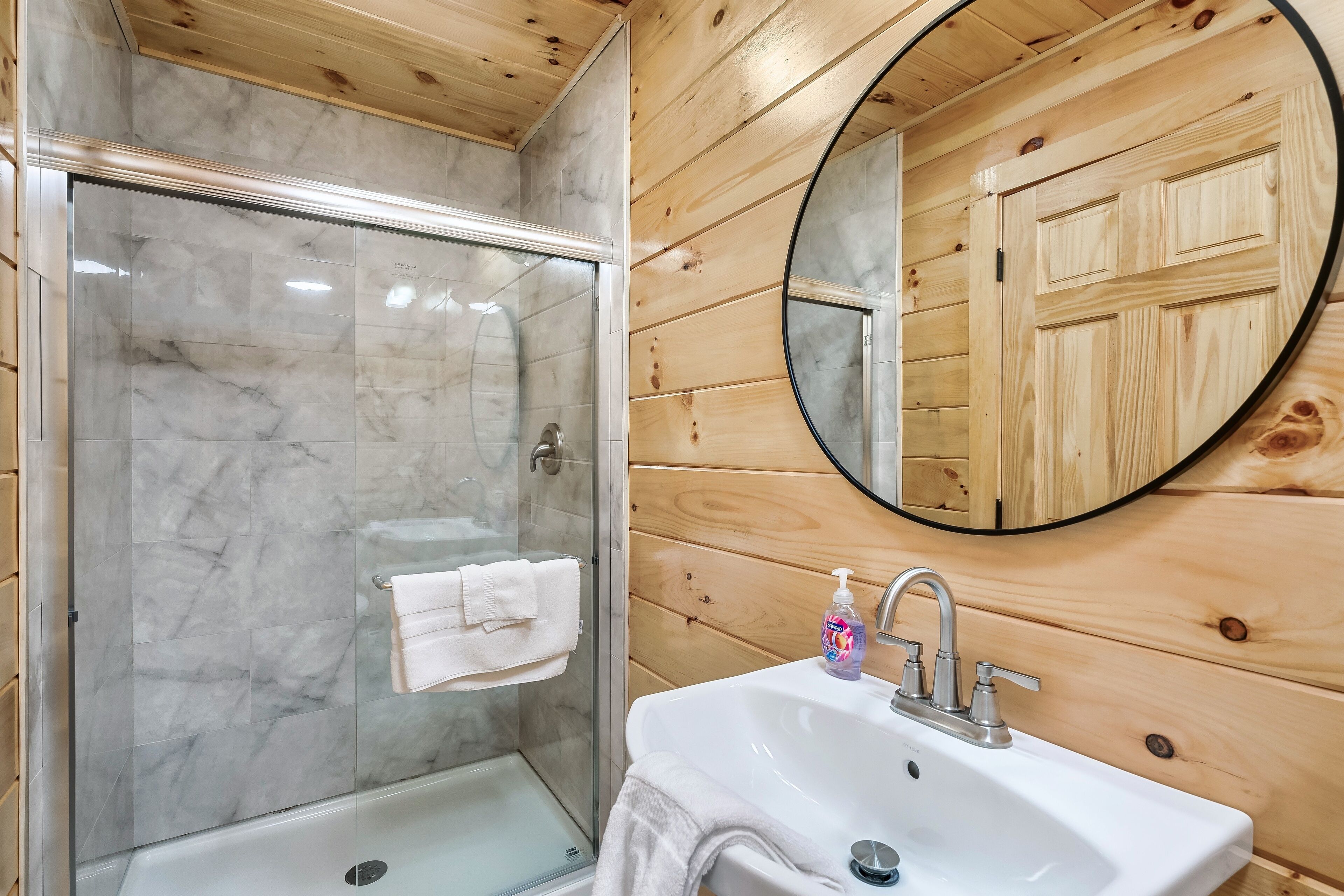 A bathroom with a glass shower, a white sink, and a wooden wall.