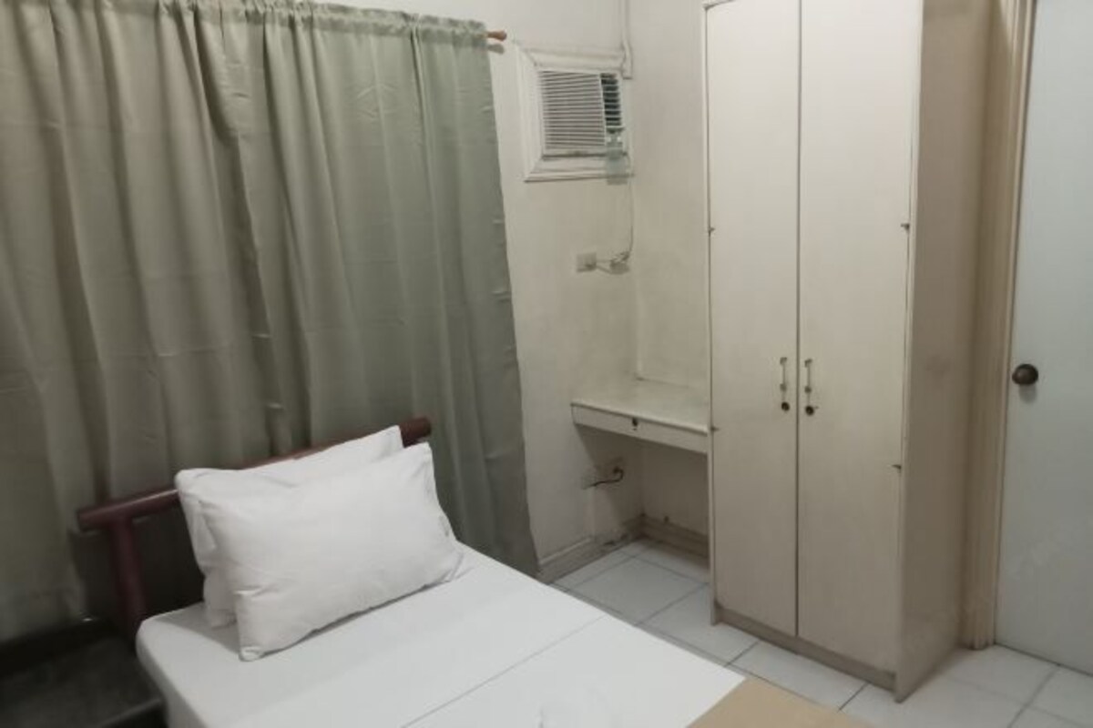 A bedroom with a bed, a wardrobe, a small desk, and a window with blinds.