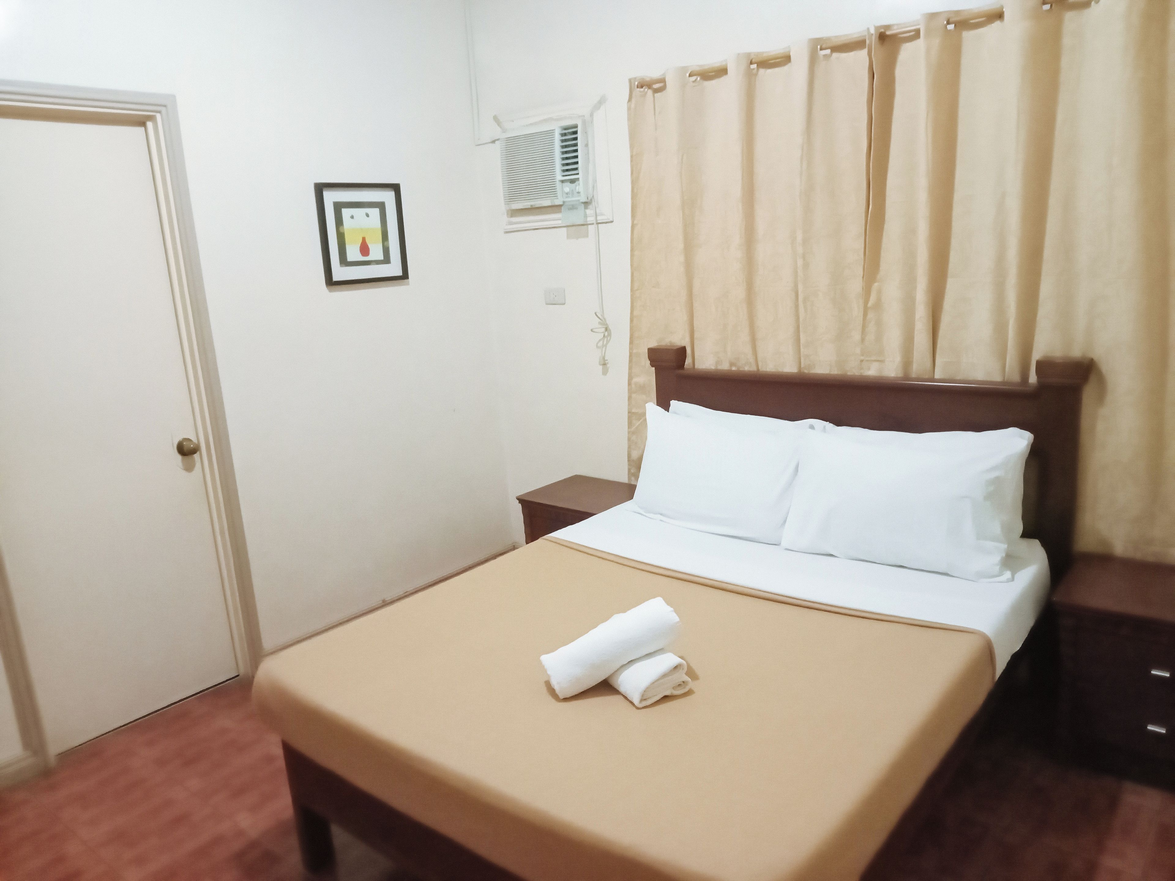 A hotel room with a bed, a nightstand, a door, and a window with curtains.