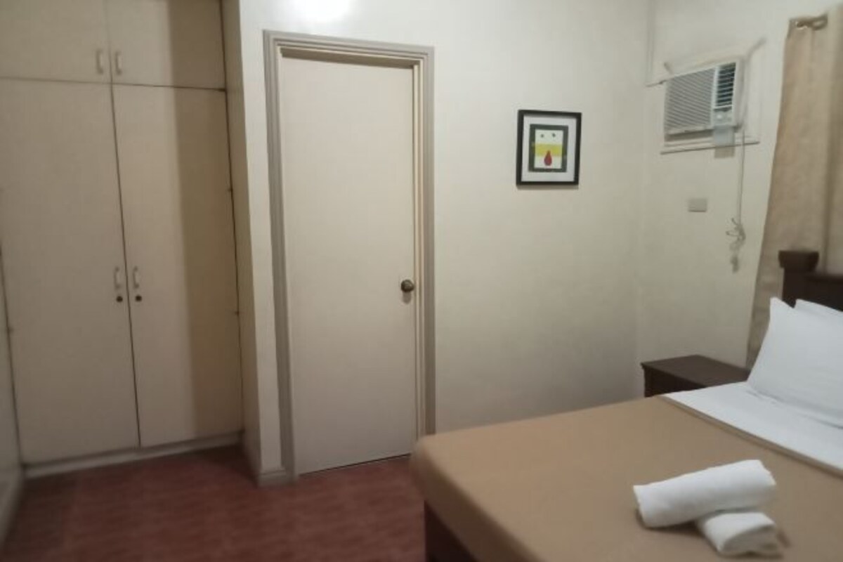 A hotel room with a bed, a wardrobe, a door, and a wall-mounted air conditioning unit.